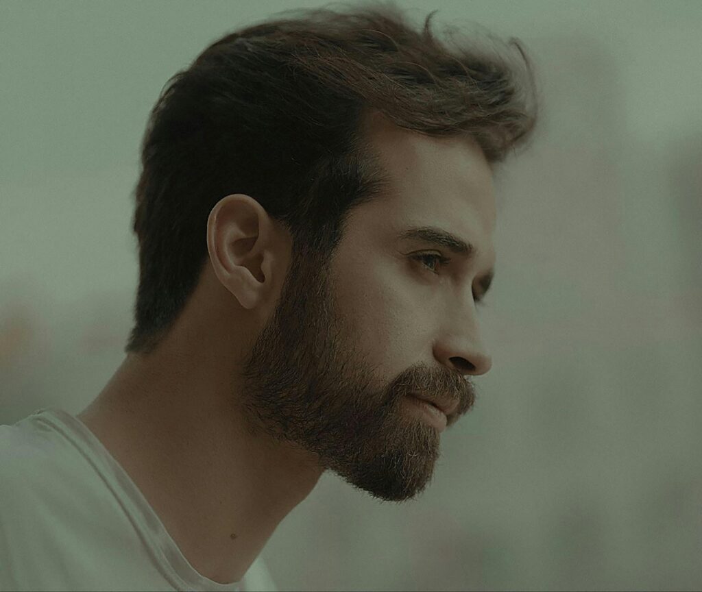 Side profile of a bearded man in an artistic setting, capturing a thoughtful expression.
