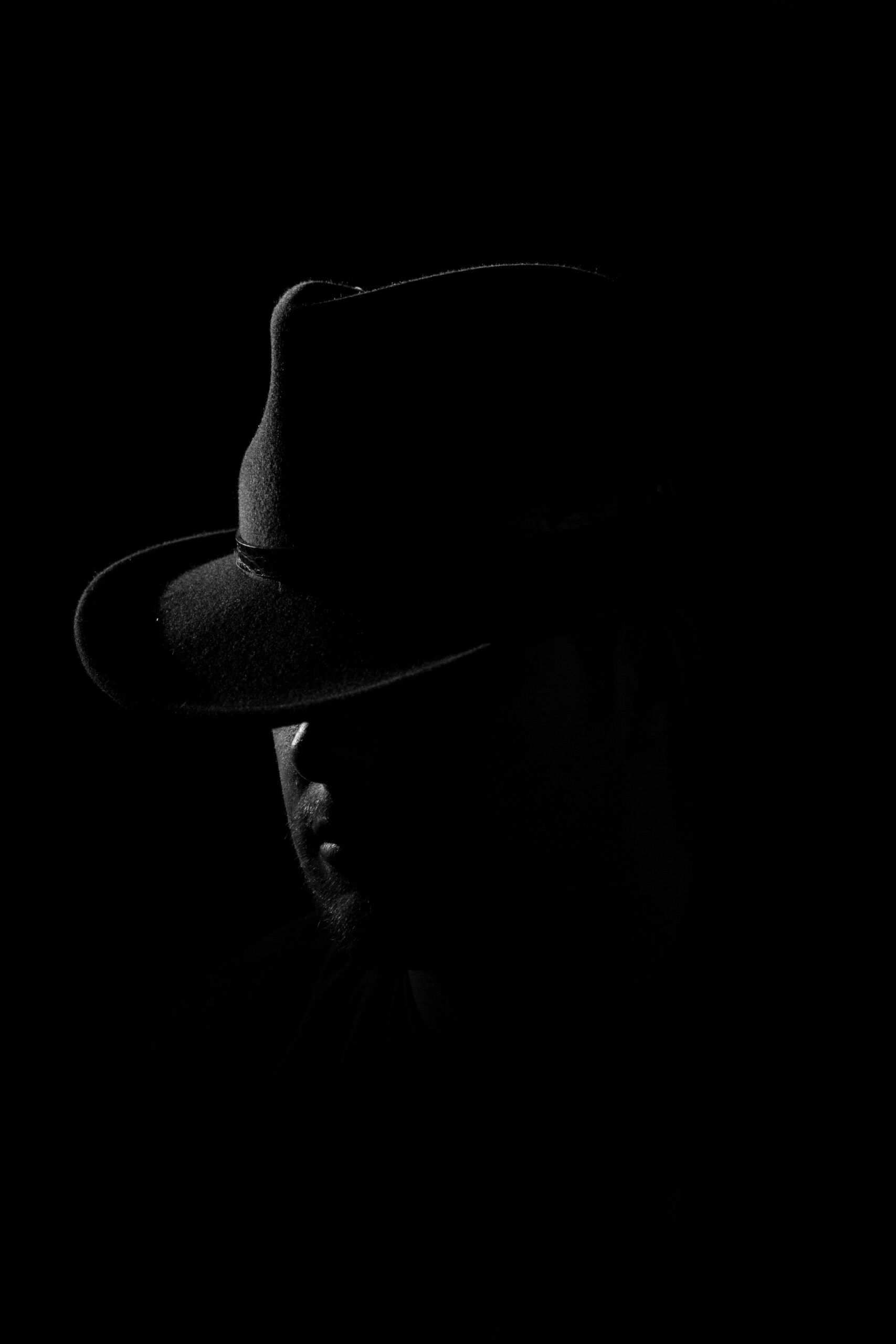 Man in shadow wearing a fedora hat with low-key dramatic lighting
