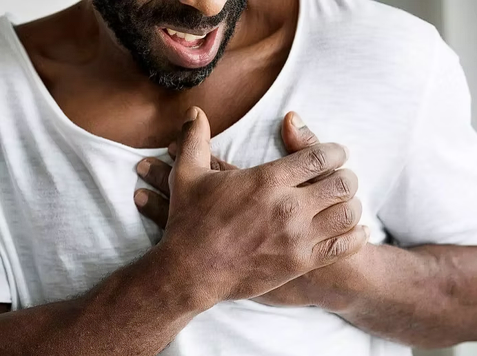 Close-up of a man clutching his chest in pain, suggesting symptoms of a possible heart attack or chest discomfort.