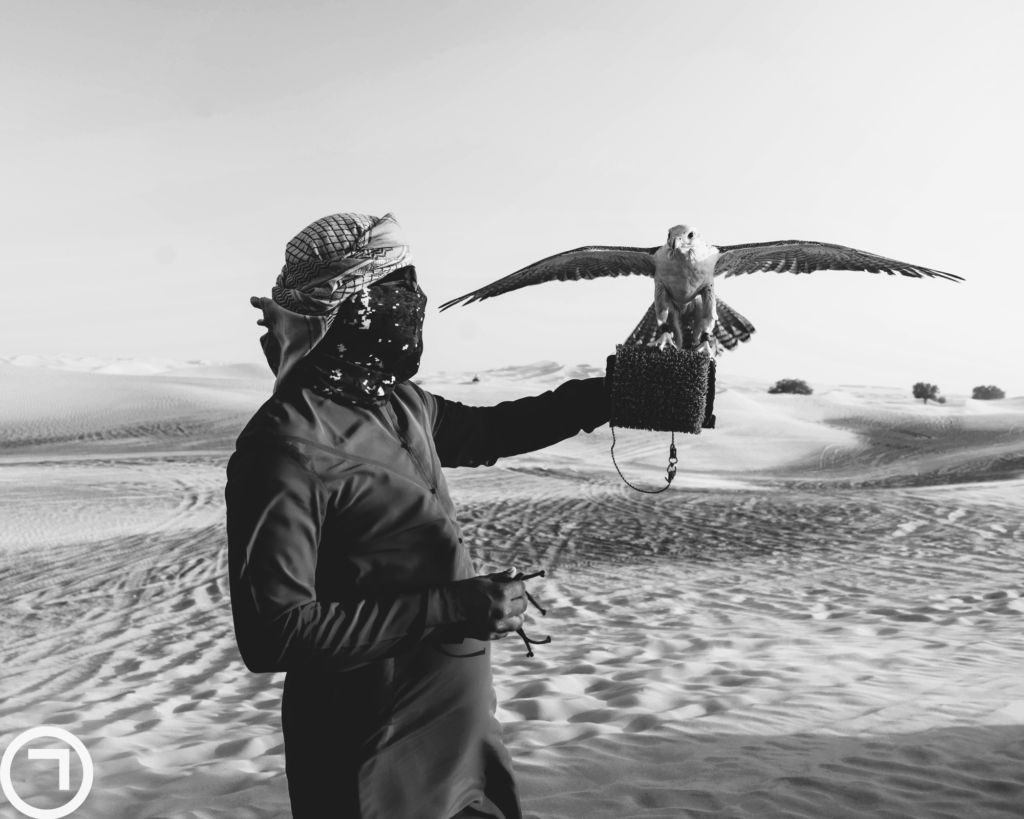  A man held a falcon on his left hand in the desert.