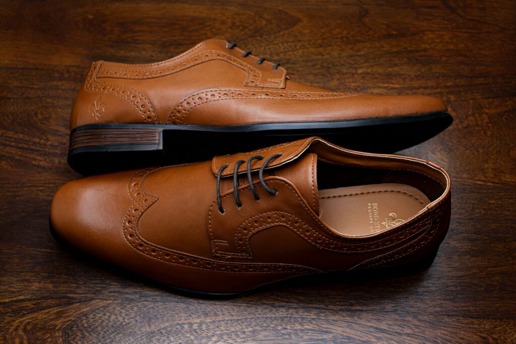 A pair of brown leather wingtip shoes with classic brogue detailing placed on a wooden surface.