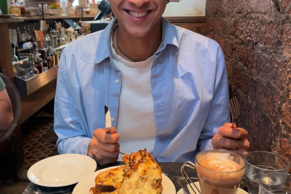 A man smiling at a café table with pastries, berries, and coffee placed in front of him in a cozy restaurant setting.