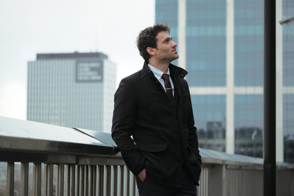 Man standing on a city bridge with skyscrapers in the background, exuding urban style.
