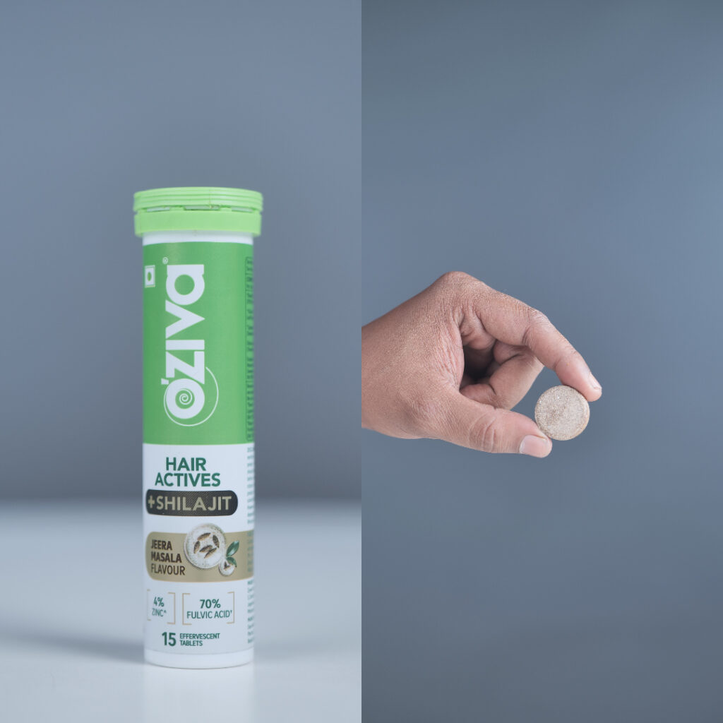 Hand holding effervescent tablet next to OZiva Hair Actives + Shilajit container