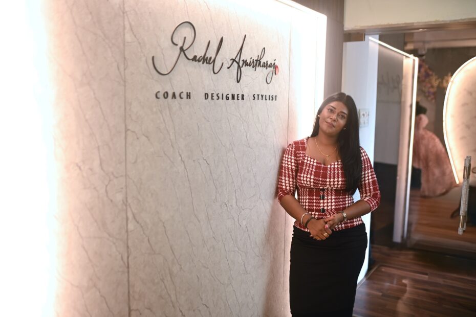 A woman standing inside a luxury bridal fashion studio beside a branded wall, showcasing a professional design environment.